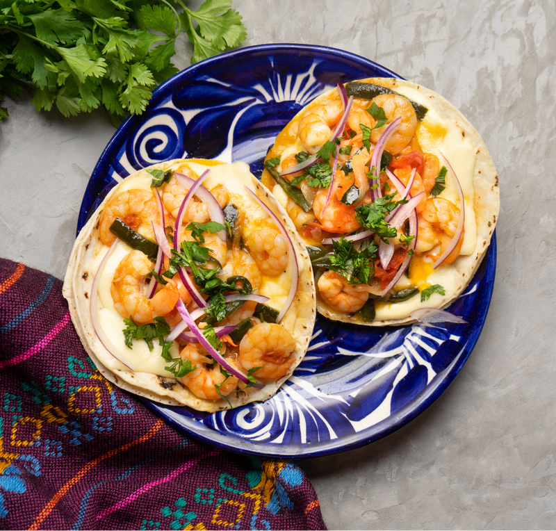 Two shrimp tacos on a blue plate with a colorful cloth underneath