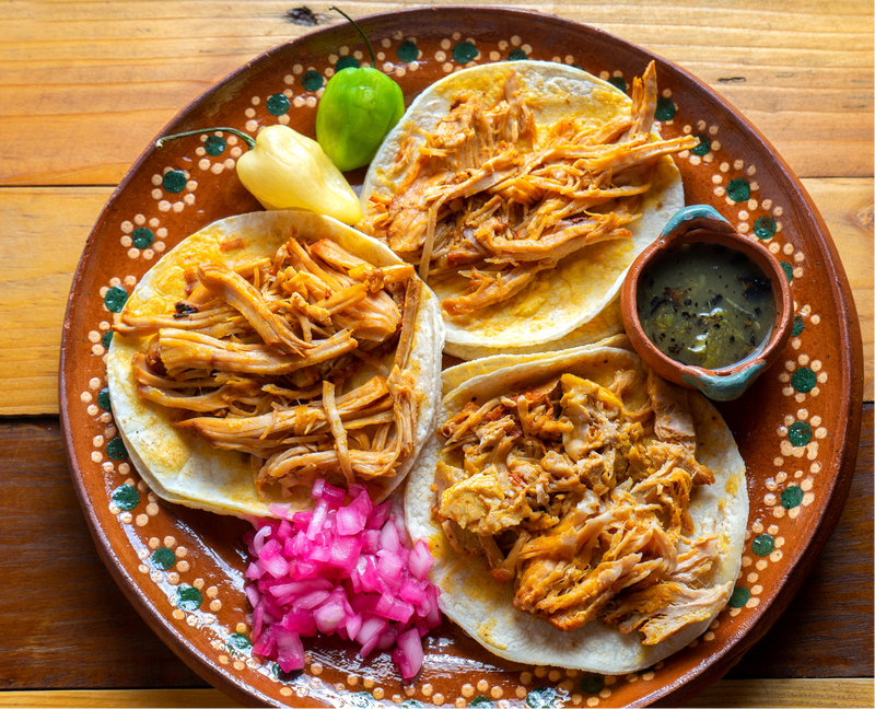 Platter of tacos with chicken pibil fillings on a decorative plate.