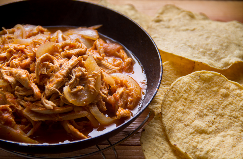 Jackfruit Tinga with onions in a pan next to tortillas on a wooden surface