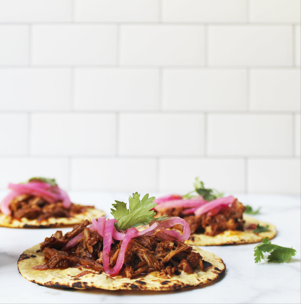 Jar of Salsaology Pibil sauce with tacos on a white background